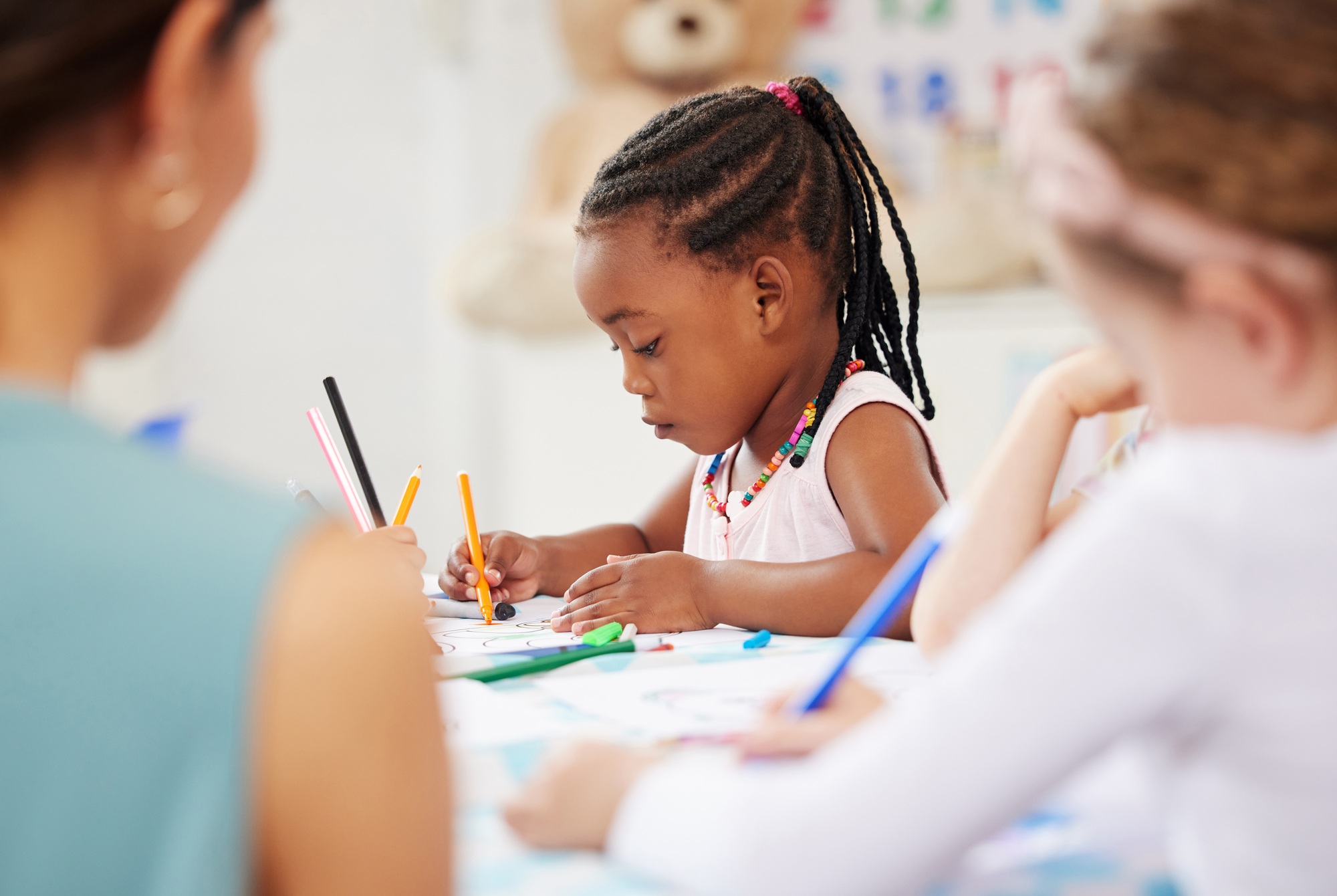 African american girl sitting at a table and colouring at pre-school or kindergarten with her fello