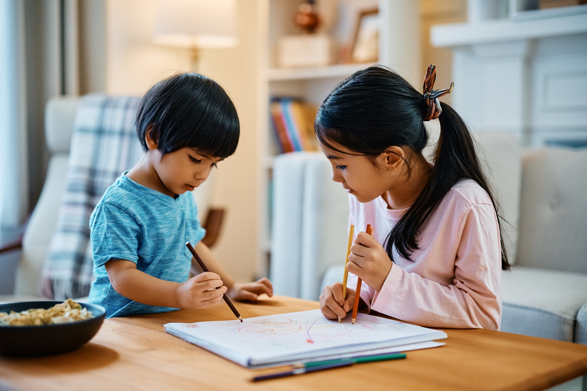 Little Asian boy enjoying in coloring on the paper with his sister at home.