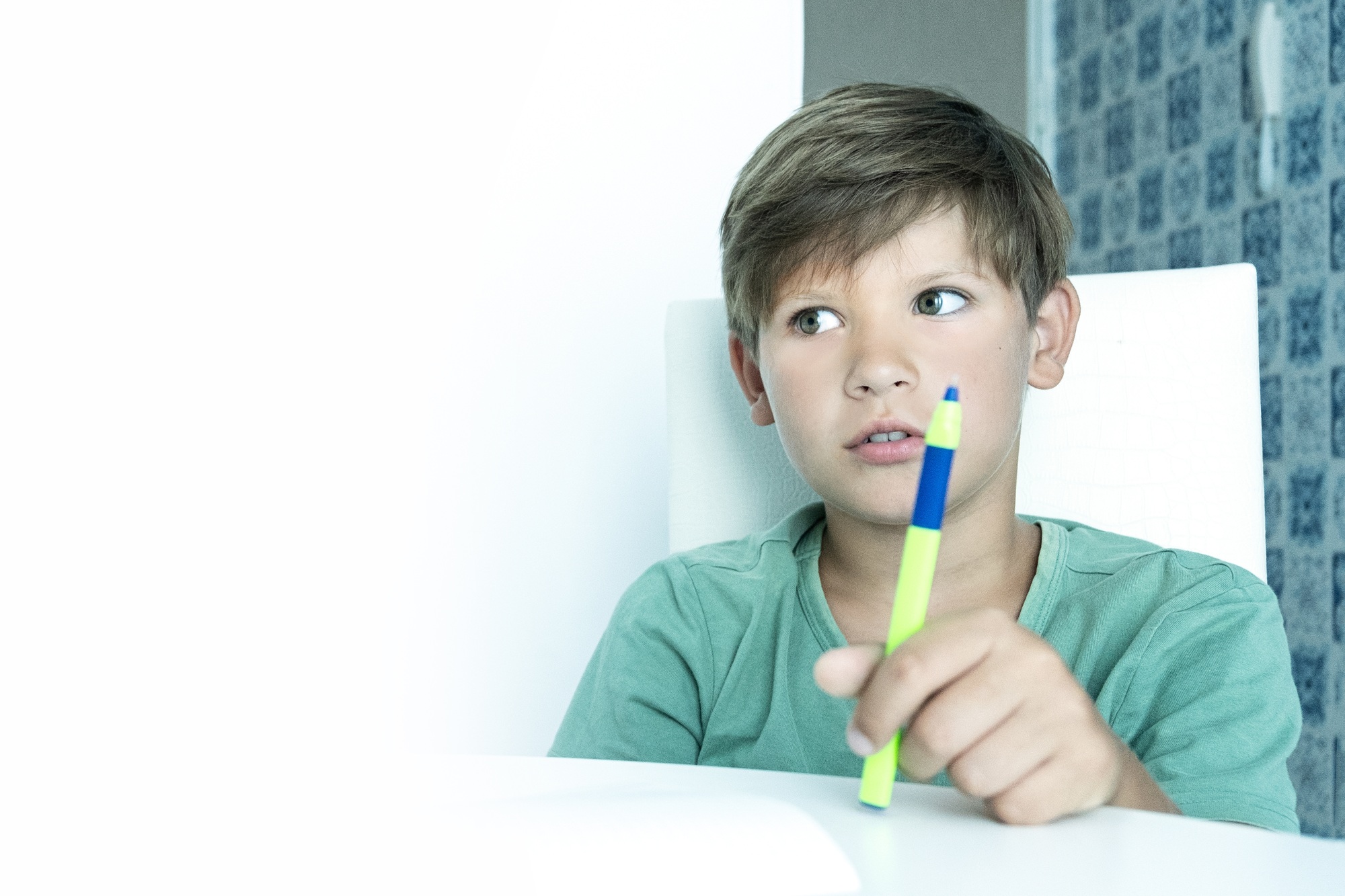 A schoolboy does his homework at home. Light background, green color. The boy is studying