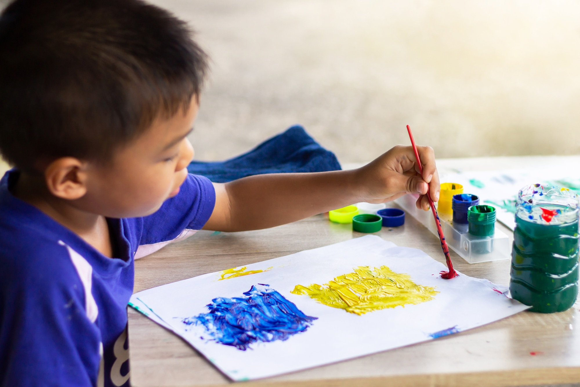 Asian student child boy drawing and painting colors on the paper in the classroom.