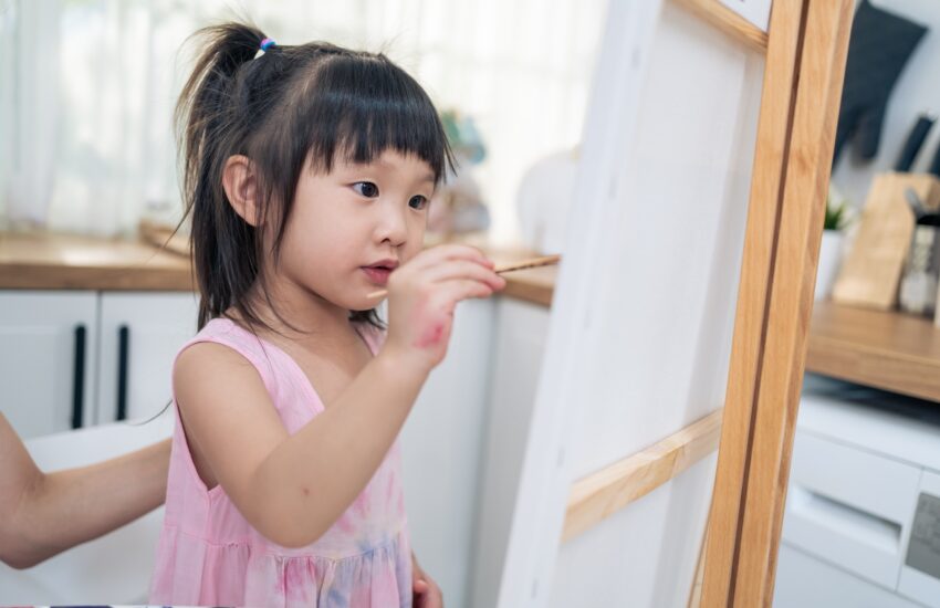 Asian young happy kid girl coloring on painting board in living room.