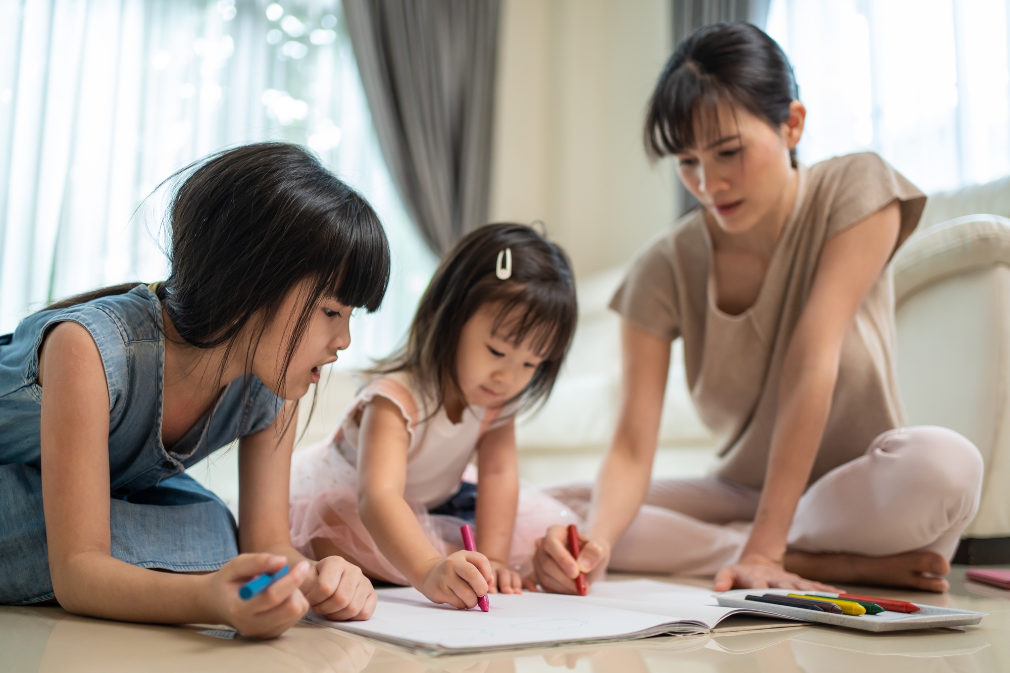 Asian young siblings girl artist having fun draw and color picture with mother on floor.