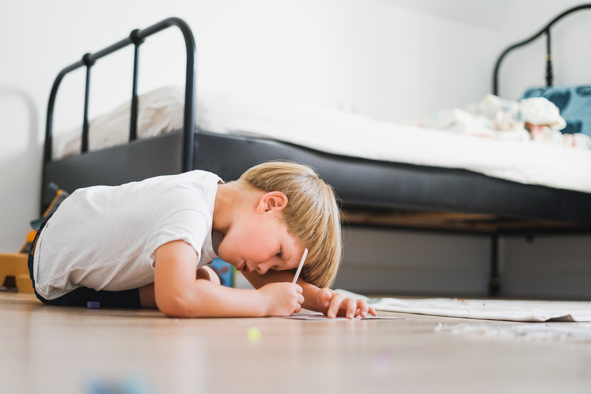 Cute blonde boy in white t-shirt draws on floor in the children room