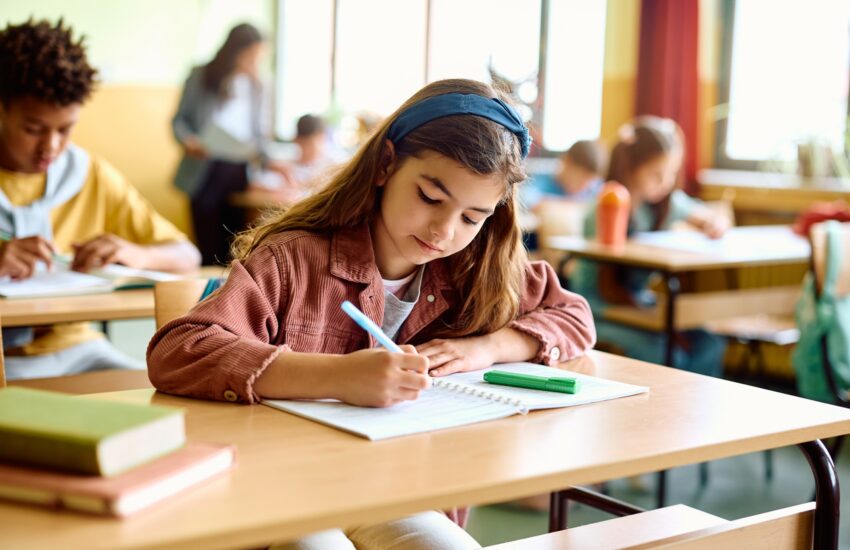 Elementary student writing in her notebook on a class at school.