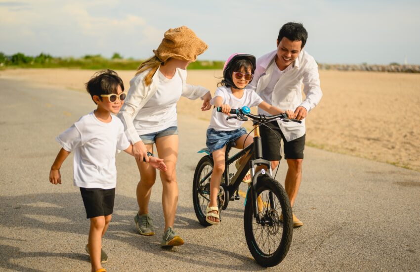 Happy family with outdoor activities riding bicycle together on beach
