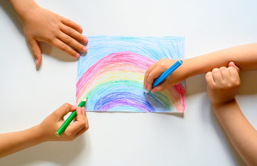 kid's hands together draw a rainbow colored pencils on white background
