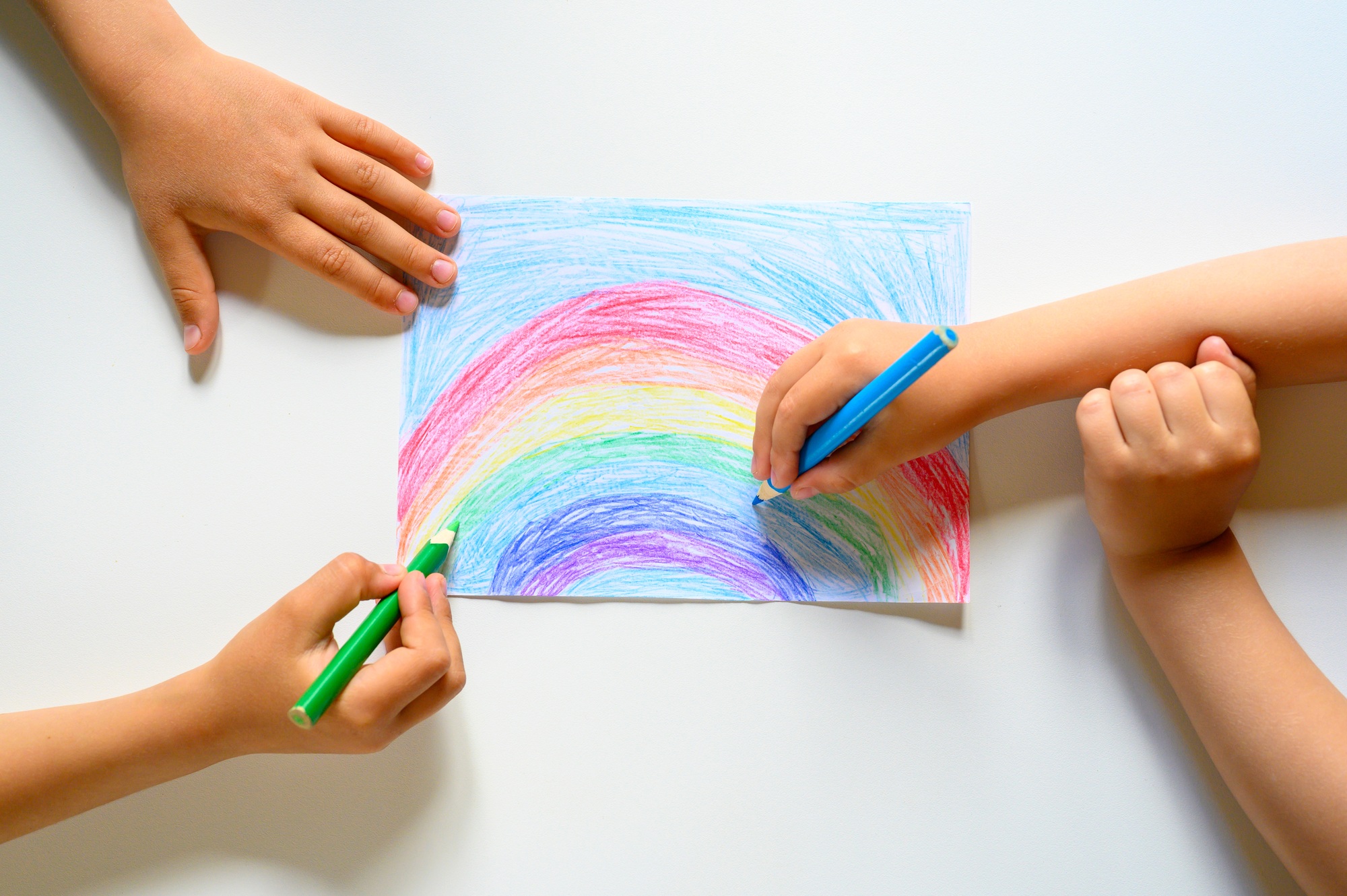kid's hands together draw a rainbow colored pencils on white background