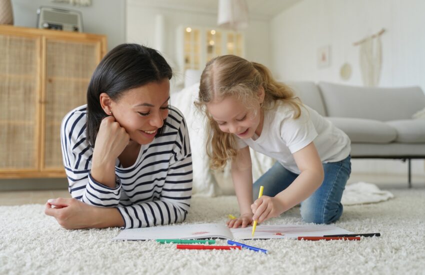 Mom, adopted child daughter draw with colorful pencils, lying on floor. Happy motherhood, adoption