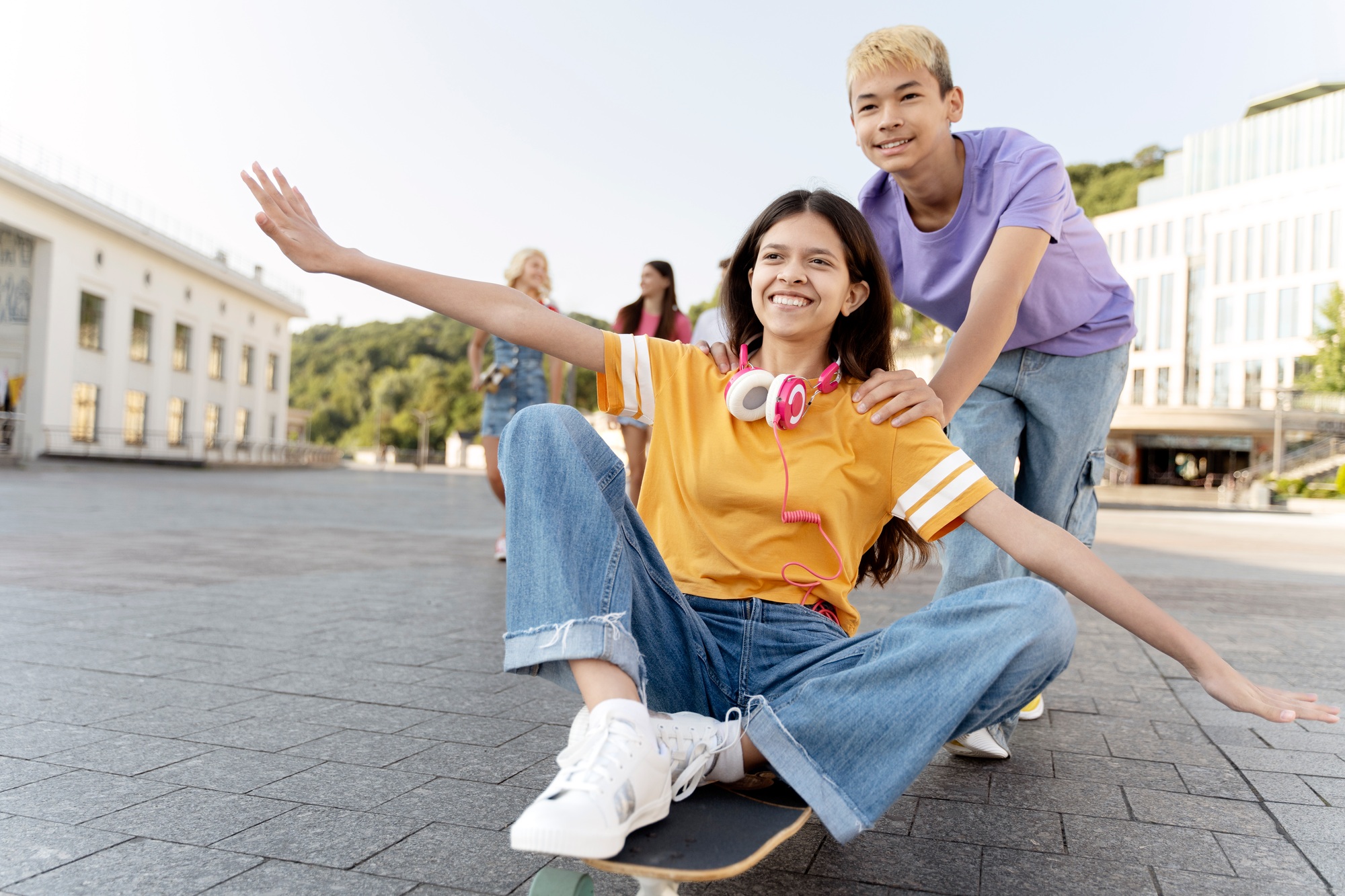 Portrait of smiling teenage friends riding on skateboard on urban street. School vacation, summer