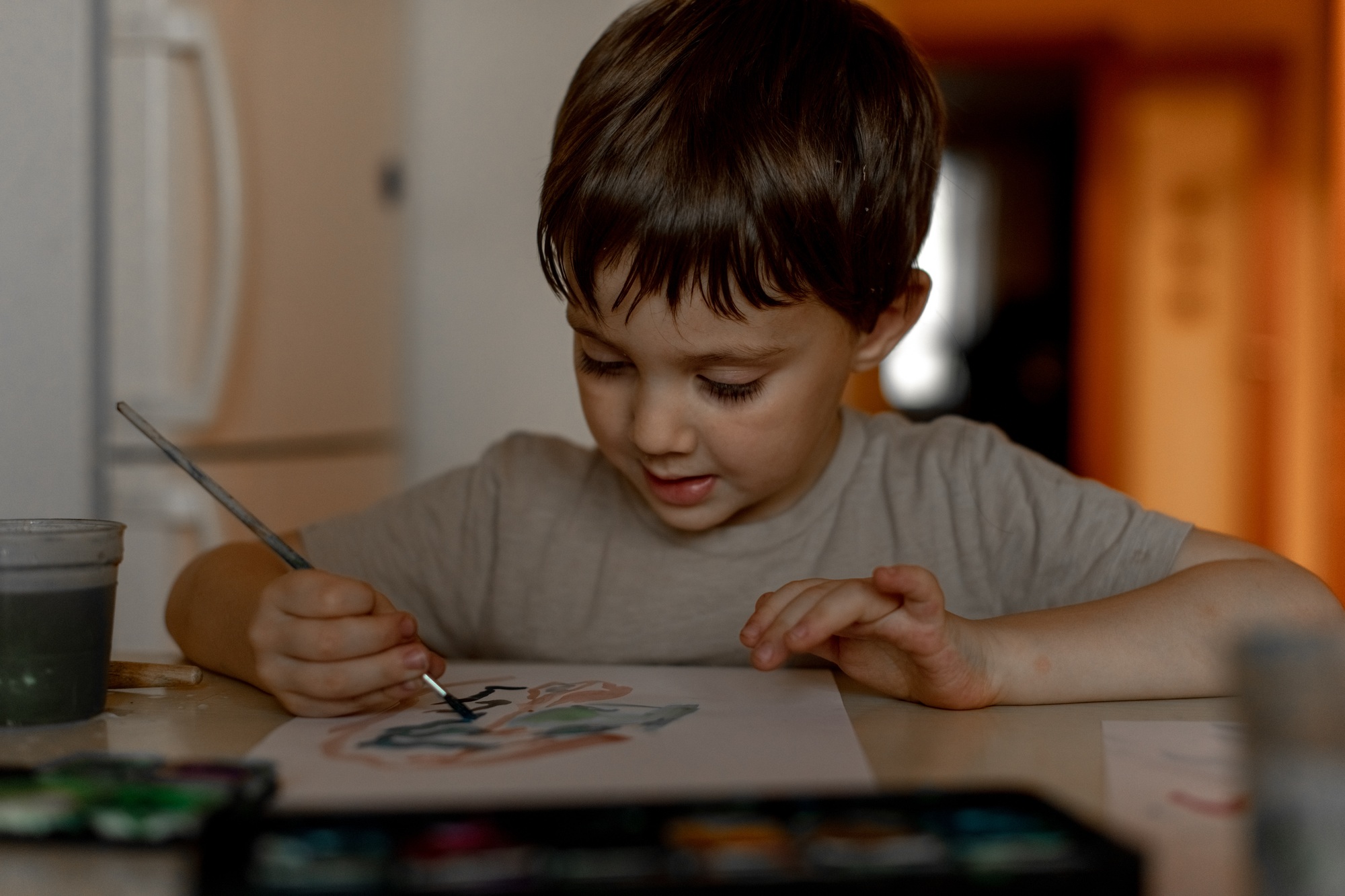 The boy draws a drawing with watercolor paints at home